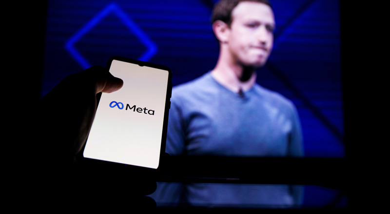 Meta logo on cellphone over a screen showing Mark Zuckerberg